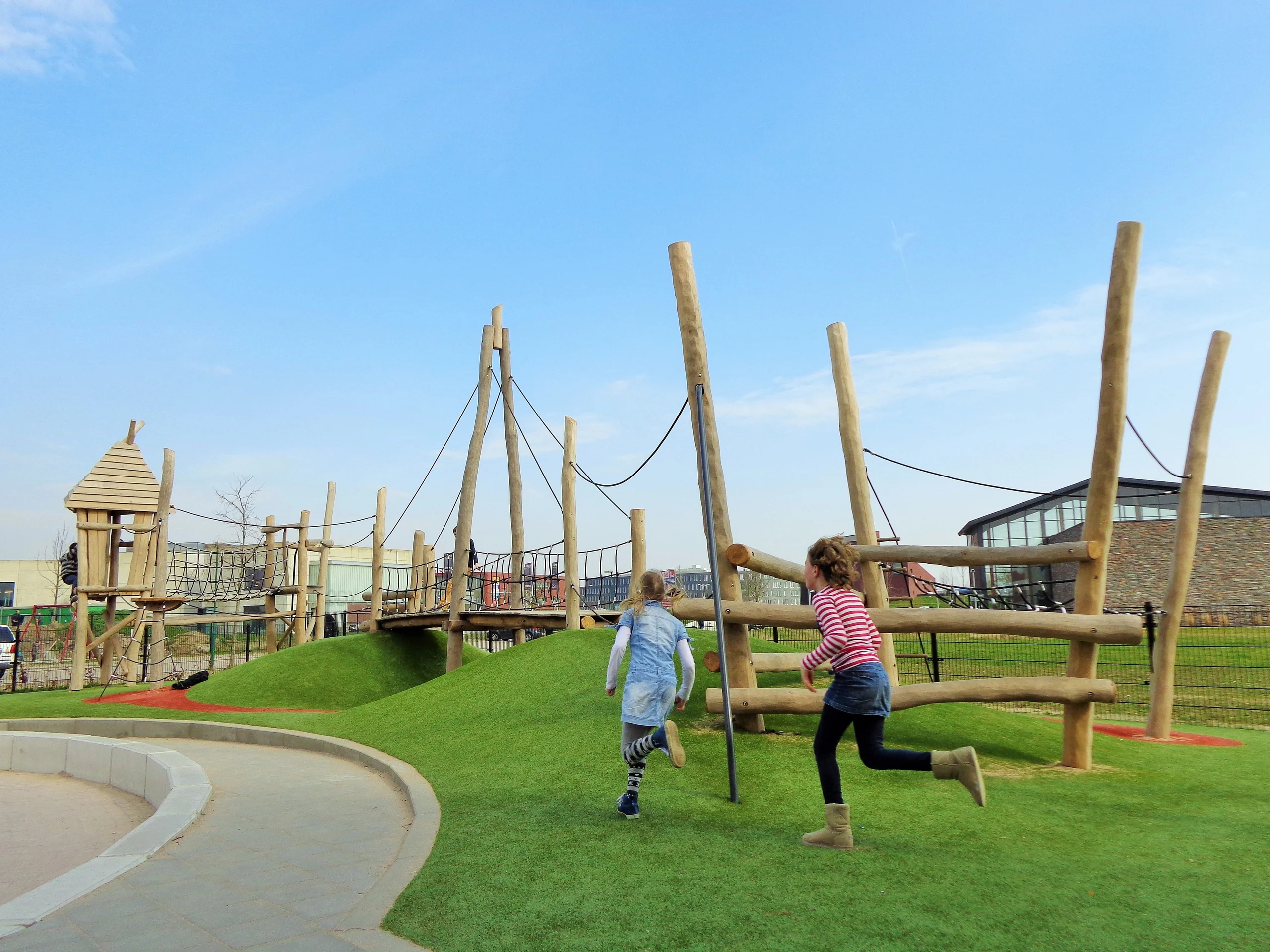 Kunstgras speelplaats met houten speeltoestellen waar twee kinderen spelen