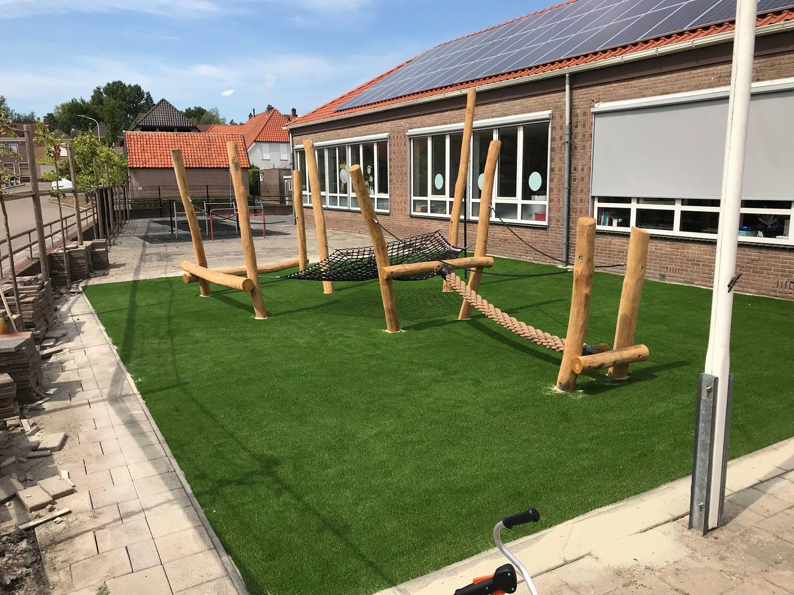 Kunstgras speelplaats met houten speeltoestellen op een schoolplein