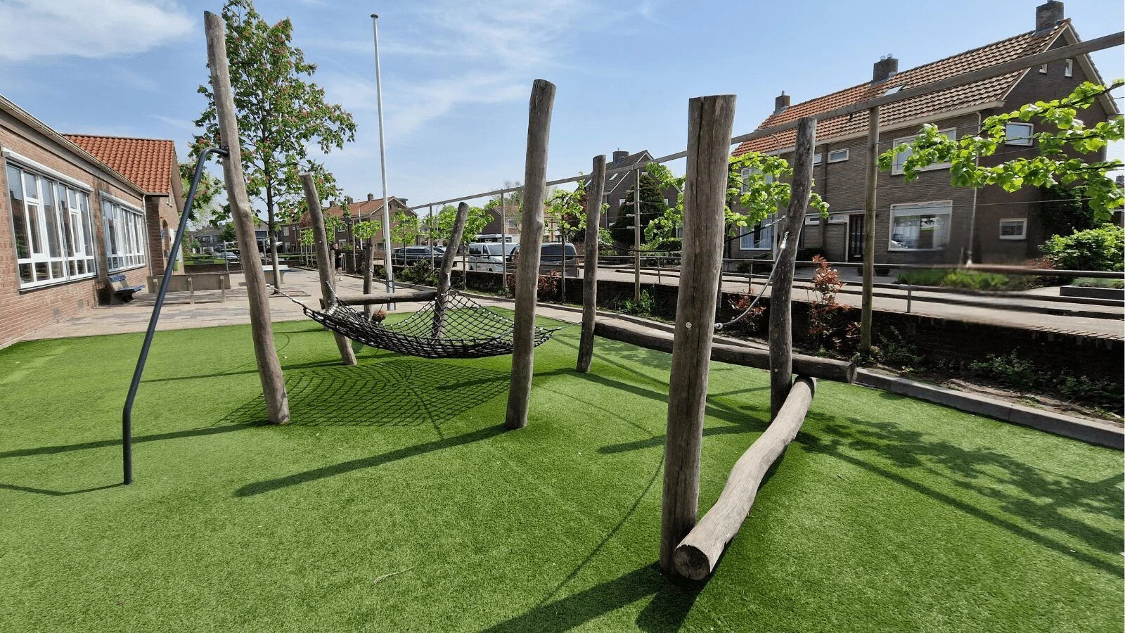Schoolplein met kunstgras, een touwnet-hangmat en houten balanceerstammen