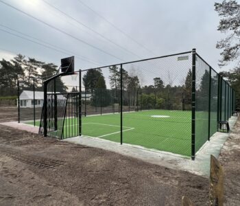 Pannaveld met groen kunstgras en hoge sportomheining